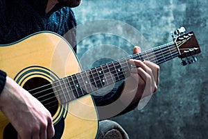 Young man playing an acoustic guitar on the background of a concrete wall photo