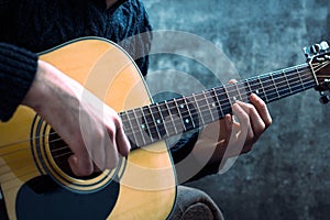 Young man playing an acoustic guitar on the background of a concrete wall