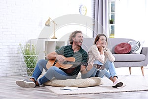 Young man playing acoustic guitar badly for displeased girlfriend in living room.