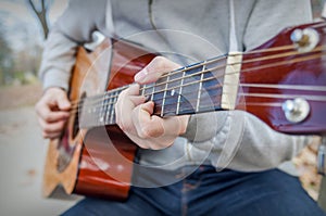 Young man playing acoustic guitar close up outdoors in autumn park