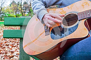 Young man playing acoustic guitar close up outdoors in autumn park