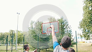 Young man playing basketball on the court outdoors with friends, throwing the ball and missing the basket