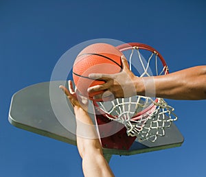 Young man playing basketball with friend against blue sky