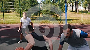 Young man playing basketball outdoors with friends and trying to score goal - leading the ball