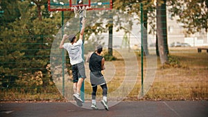 Young man playing basketball on the sports ground with friend - dribbling, avoiding his opponent and throwing a ball -