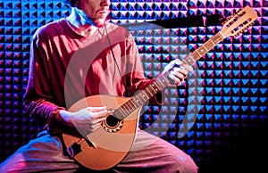 Young man playing on the bouzouki in sound recording studio.