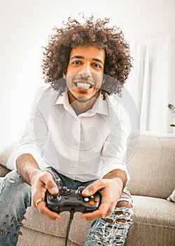 Young man playing computer game alone at home. Shuggy gamer smiles holding joystick. Self isolation concept. Dutch angle