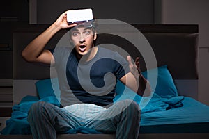 The young man playing computer games at night in bed