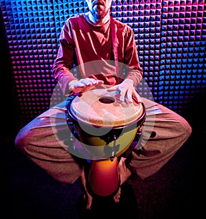 Young man playing on djembe in sound recording studio.