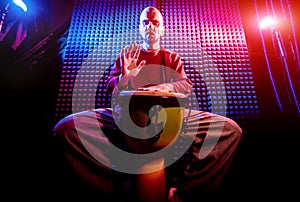 Young man playing on djembe in sound recording studio.