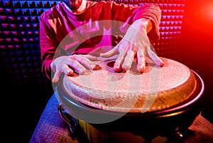 Young man playing on djembe in sound recording studio.