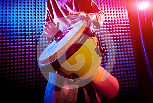 Young man playing on djembe in sound recording studio.