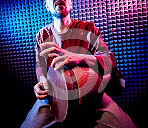 Young man playing on djembe in sound recording studio.