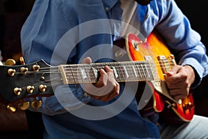 Young man playing guitar, close up view, dark background