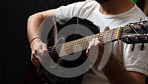 Young man playing guitar, close up view, dark background