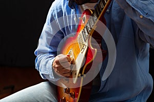 Young man playing guitar, close up view, dark background