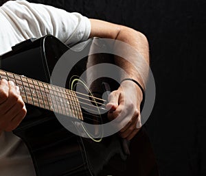Young man playing guitar, close up view, dark background