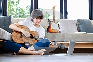 Young man playing guitar and learning a new song with laptop, guitarist musician lifestyle