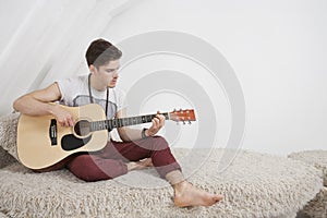 Young man playing guitar while sitting on fur sofa