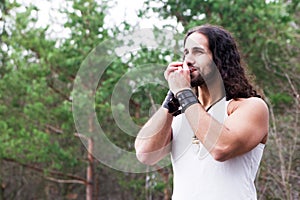 Young man playing the harmonica in a forest glade.