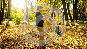 Young man playing and havng fun with his little son in autumn park