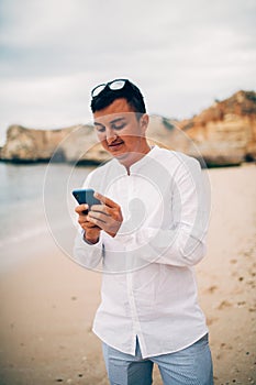 Young man playing with phone on a beach in Portugal at sunrise