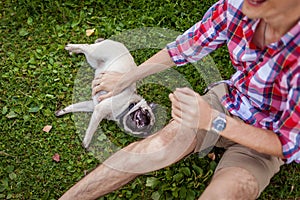 Young man playing with pug dog sitting on grass. Happy puppy having fun with master