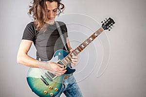 Young man is playing solo an electric guitar and waving his long hair. Emotional performance of rock and roll