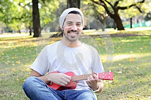 Young man playing the ukelele in a park.