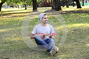 Young man playing the ukelele in a park.