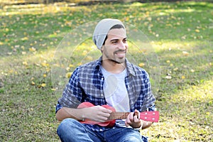 Young man playing the ukelele in a park.