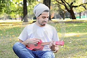 Young man playing the ukelele in a park.