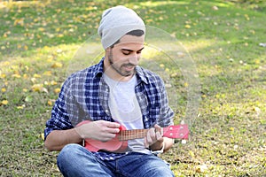 Young man playing the ukelele in a park.