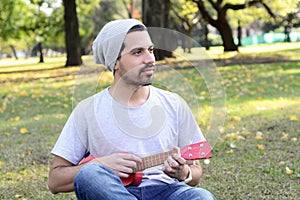 Young man playing the ukelele in a park.