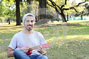 Young man playing the ukelele in a park.