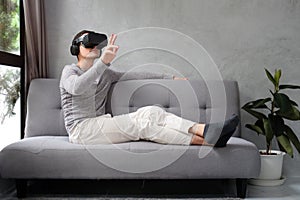 Young man playing video games in virtual reality headset while sitting on sofa at home