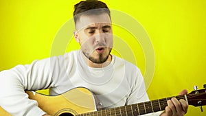 A young man plays the guitar and sings a song. Handsome Caucasian man in a white sweatshirt sings with a guitar. Yellow