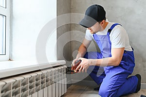 young man plumber checking radiator while installing heating system in apartment