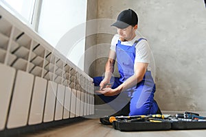 young man plumber checking radiator while installing heating system in apartment