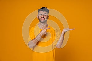 Young man pointing finger and holding copyspace palm isolated over yellow background