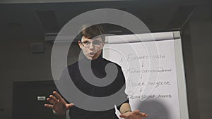 Young man pointing at flipchart while giving presentation to his colleagues