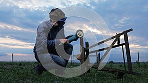 A young man polishes a metal angle grinder at sunset. Beautiful sky behind the worker.