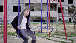 Young man in a poor state of health sits on a swing