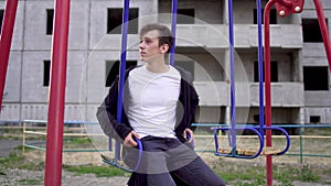 Young man in a poor state of health sits on a swing