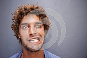 Young man, portrait and silly face for funny or goofy expression against a gray wall background. Male with crazy humor