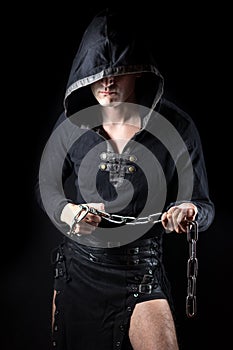 Young man posing in hooded gothic clothes with chain in hands