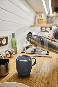 Young man pouring hot coffee into cup from thermos travelling with trailer van