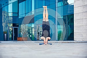 Young man practices headstand yoga asana Sirsasana pose outdoors against the background of a modern city