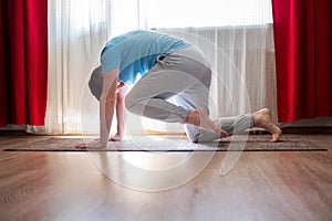 Young man practices yoga asana chakravakasana or bird pose at the living room