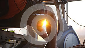 Young man practicing on the exercise bike simulator at home by window looking on the city during sunset with lens flare